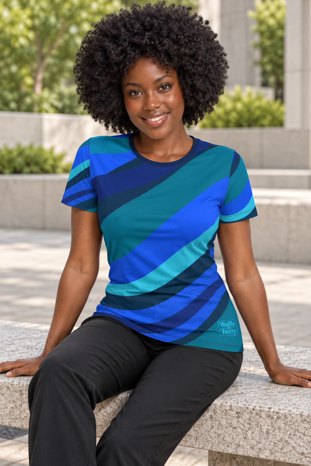 AI styling illustration: Simone seated on an outdoor bench in the Cobalt Current women's tee, showing the navy neckline and lower-left front blue box logo. Fabric and fit vary by selected option.