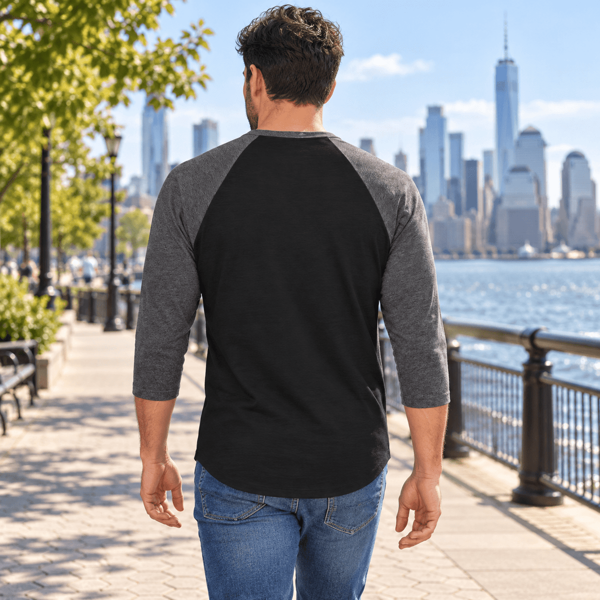 Illustrative model wearing the Black/Heather Charcoal New York Wins raglan shirt beside the New York waterfront, plain back view.