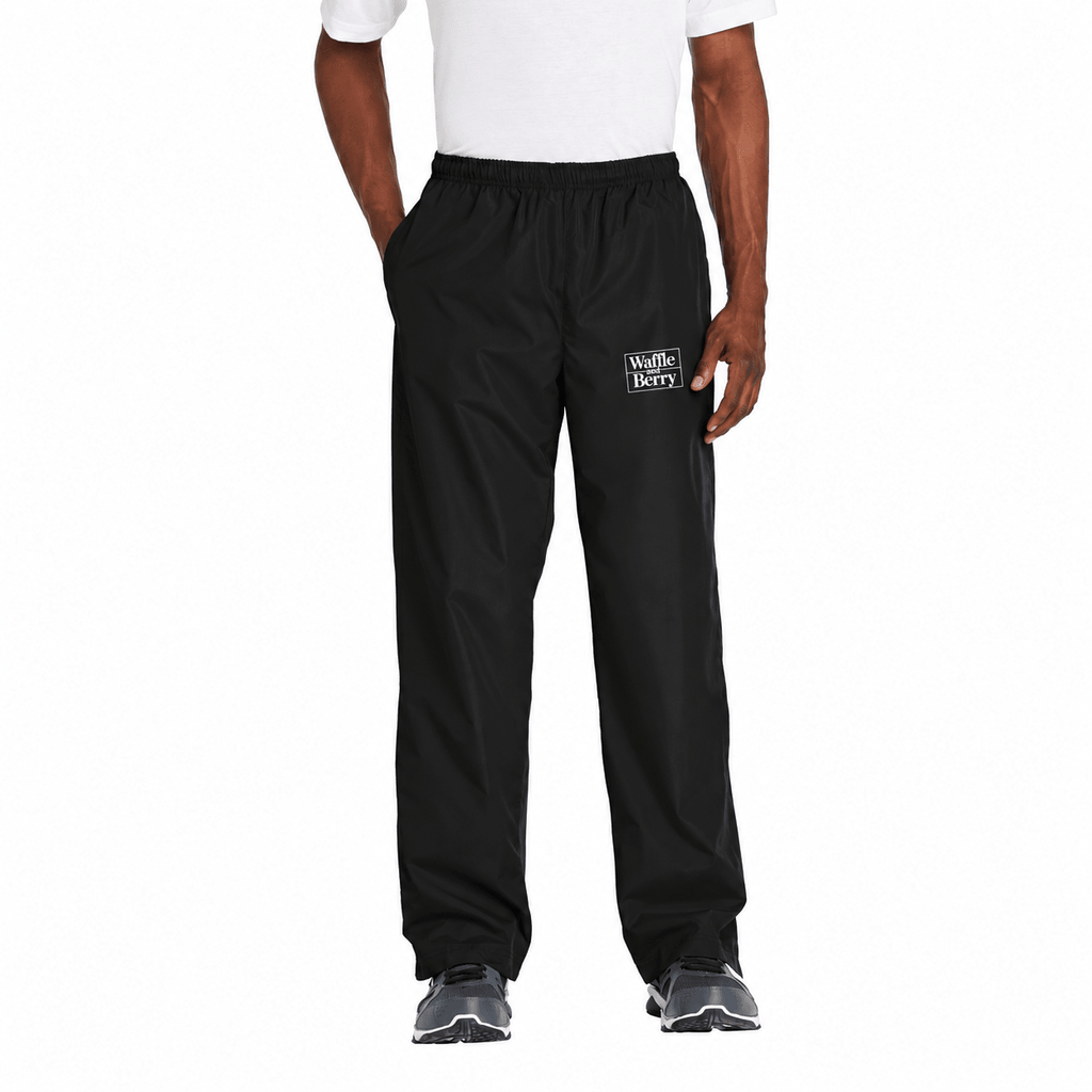AI-edited supplier photograph: black Waffle and Berry wind pants with a white wearer-left-thigh logo. Digitally decorated visualization, not a physical printed sample.