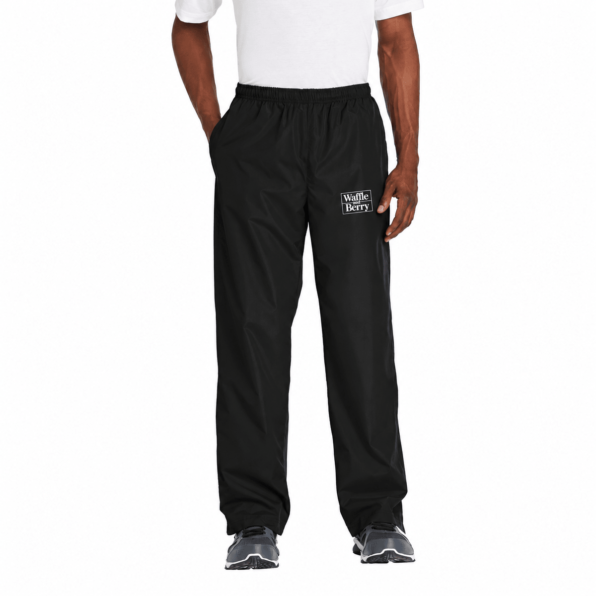 AI-edited supplier photograph: black Waffle and Berry wind pants with a white wearer-left-thigh logo. Digitally decorated visualization, not a physical printed sample.